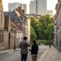 Two people on a quiet Brussels street, map and phone in hand, considering options between old buildings and modern skyline.