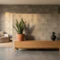 A modern living room with a textured concrete block wall, wooden console, snake plant, and ceramic vase, bathed in soft natural light.