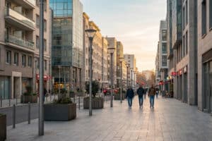 Scène de rue urbaine moderne en France au crépuscule. Des piétons marchent le long de bâtiments contemporains sous une lumière douce.