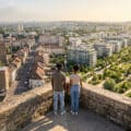 Young couple on elevated viewpoint overlooking Champigny-sur-Marne's contrasting urban landscape: dense old buildings vs. modern green areas with river.