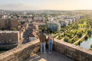 Young couple on elevated viewpoint overlooking Champigny-sur-Marne's contrasting urban landscape: dense old buildings vs. modern green areas with river.