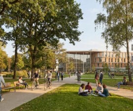 Étudiants se promenant, faisant du vélo et travaillant sur la pelouse devant des bâtiments modernes et arborés.