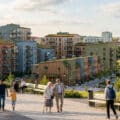 Vue d'un quartier résidentiel moderne avec des immeubles colorés et des habitants se promenant dans un parc.