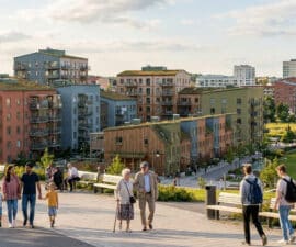 Vue d'un quartier résidentiel moderne avec des immeubles colorés et des habitants se promenant dans un parc.