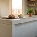 Îlot de cuisine minimaliste en béton brut avec pain et citrons, dans une cuisine ouverte lumineuse.