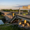 Une section de pont autoroutier effondrée dans un canal avec des inspecteurs en gilets de sécurité sur place.