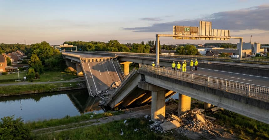 Une section de pont autoroutier effondrée dans un canal avec des inspecteurs en gilets de sécurité sur place.