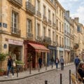 Rue pavée avec commerces, passants et terrasse de café dans une ville historique française.