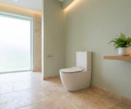 WC moderne dans une salle de bain lumineuse aux murs vert sauge et sol en pierre beige.